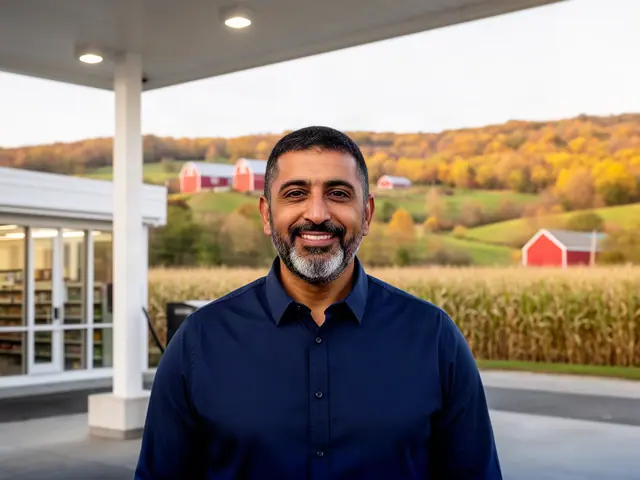 A smiling gas-station owner under the canopy with autumn hills and red barns beyond.